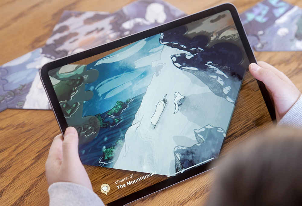 Close up shot of an ipad scanning one of the puzzle piece. The screen shows a slightly different scene than the one shown on the card : a little bear is going up a snowy mountain, accompanied by a little arctic fox. He is holding a feather.