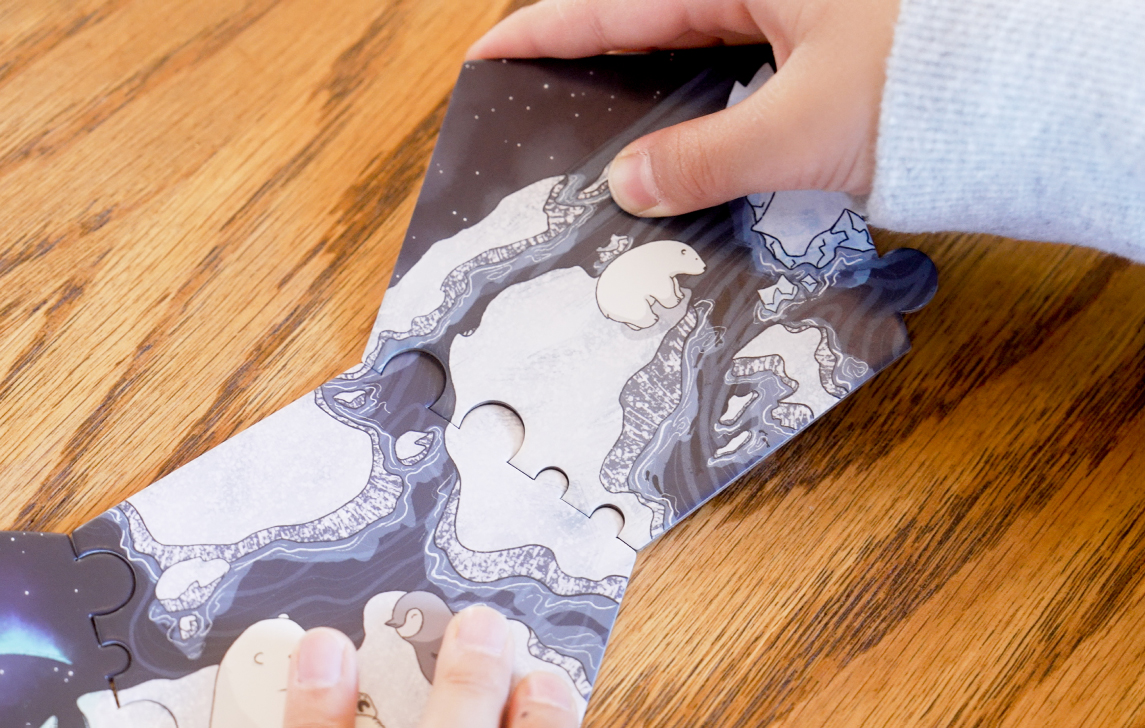 close up shot of kid's hands connecting puzzle pieces. The piece he is holding features a little polar bear standing on the edge of an icefloe, looking scared.