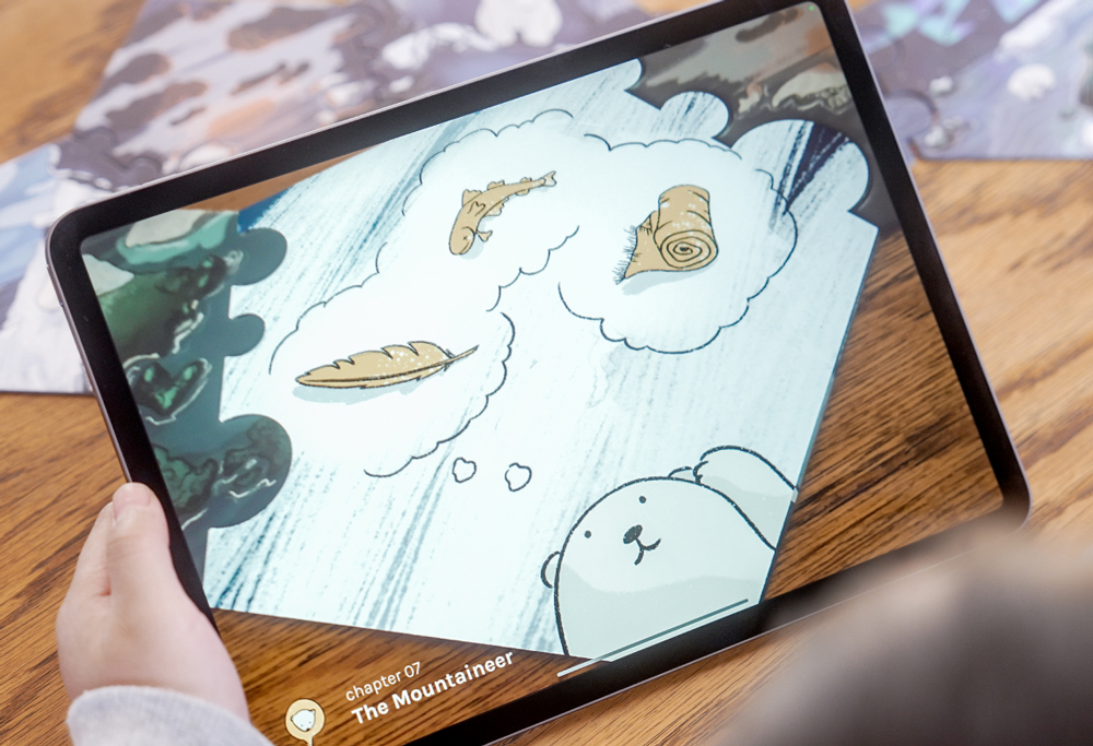 Close up shot of an ipad, scanning one of the puzzle pieces and showing a little bear thinking. A fish, a blanket and a feather are visible and can be selected.